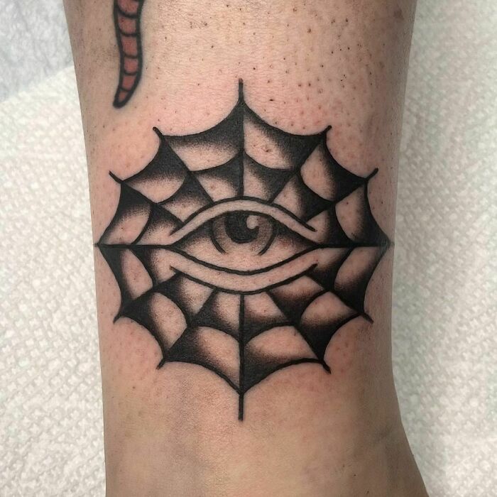 American traditional tattoo featuring an eye within a spiderweb design on forearm.