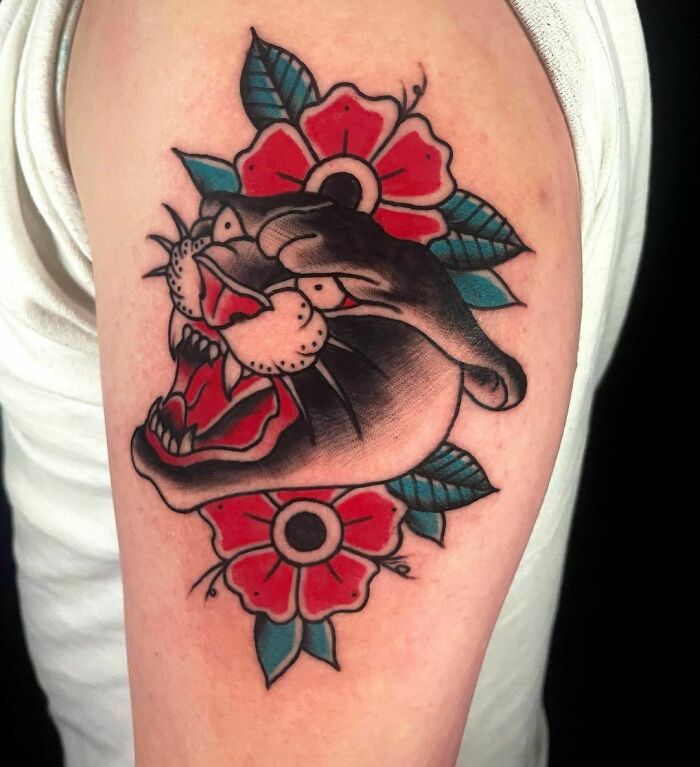 American Traditional tattoo featuring a roaring panther and vibrant red flowers on an arm.