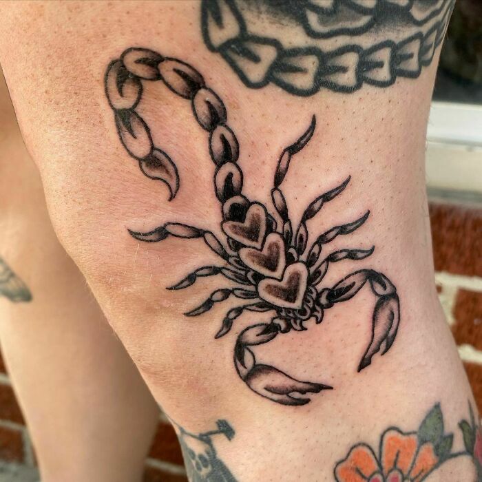 Traditional American scorpion tattoo design with heart motifs on a person's knee.