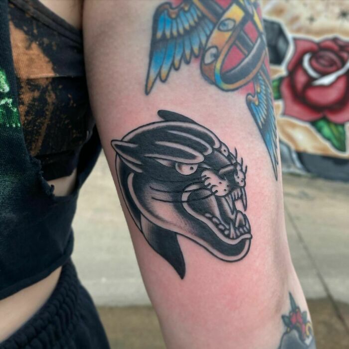 Black panther American traditional tattoo on upper arm against a colorful background.