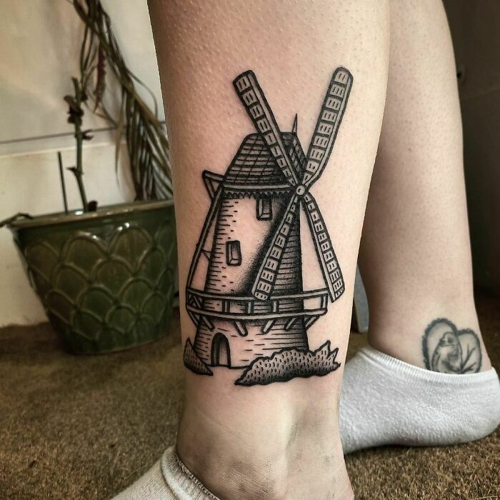 American traditional tattoo of a windmill on a person's leg, showcasing bold black lines and classic design elements.