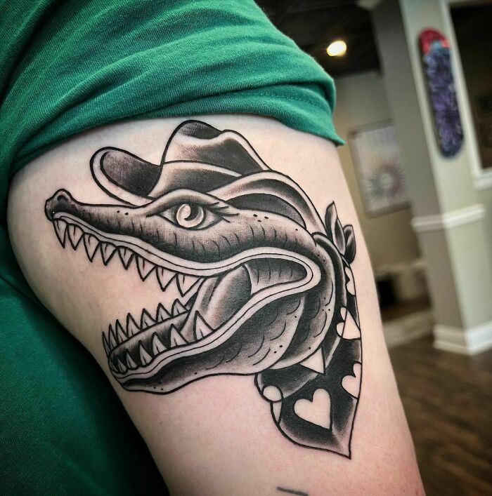 American traditional tattoo of an alligator head wearing a hat, inked on an arm for a timeless look.