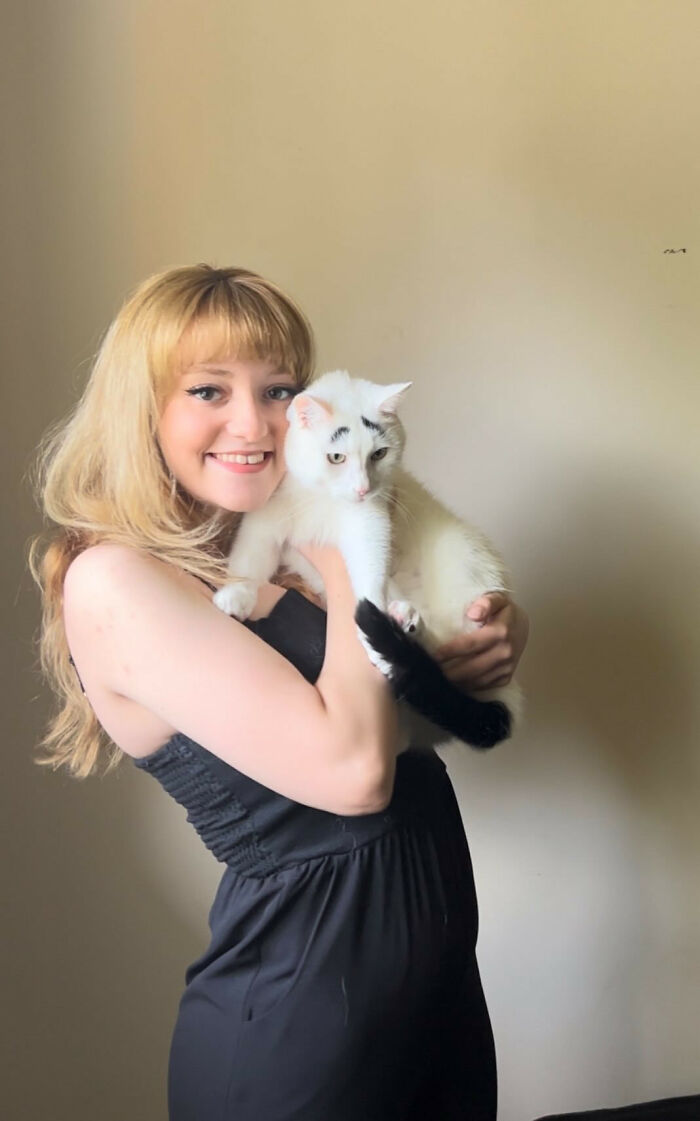 Woman hugging white cat with eyebrows 