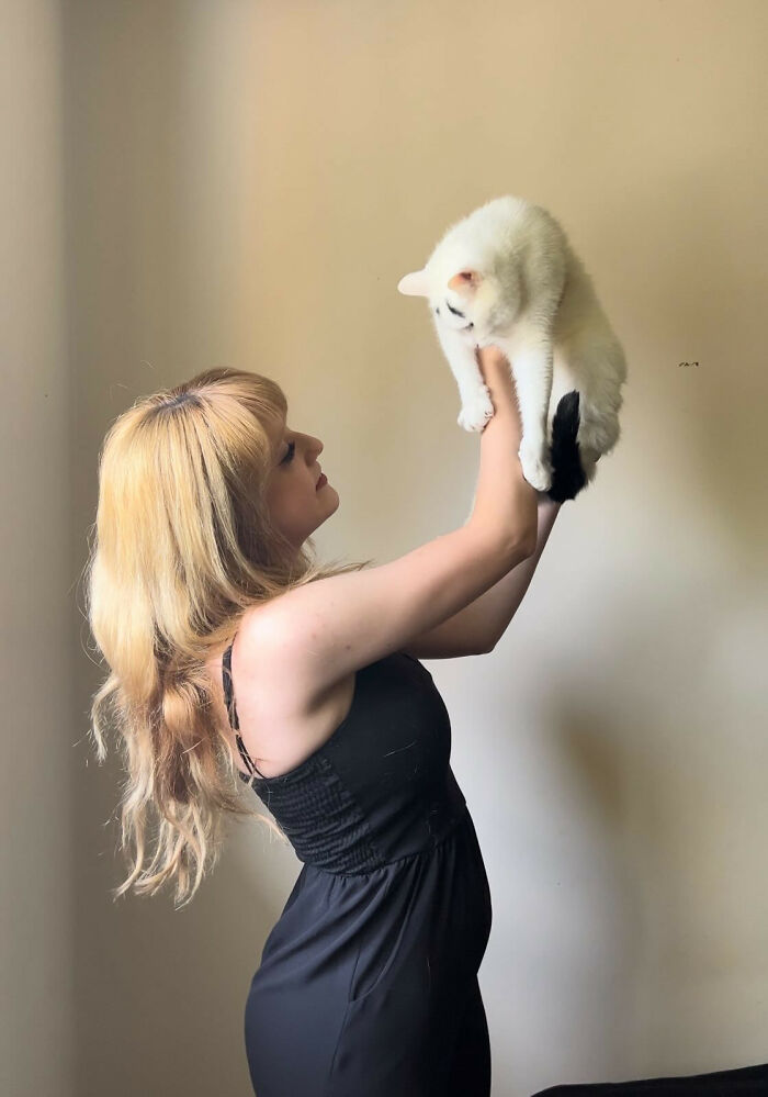 Woman holding a white cat with a black tail and eyebrows 