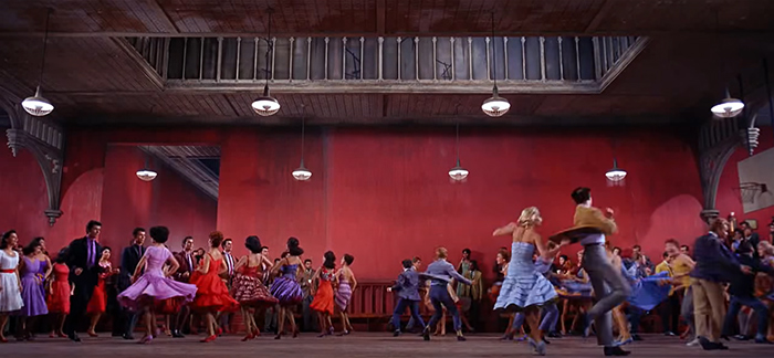 Characters from West Side Story dance in spacious place with red walls