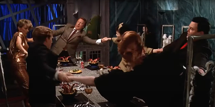 The characters of Beetlejuice hold hands at the dinner table and swinging
