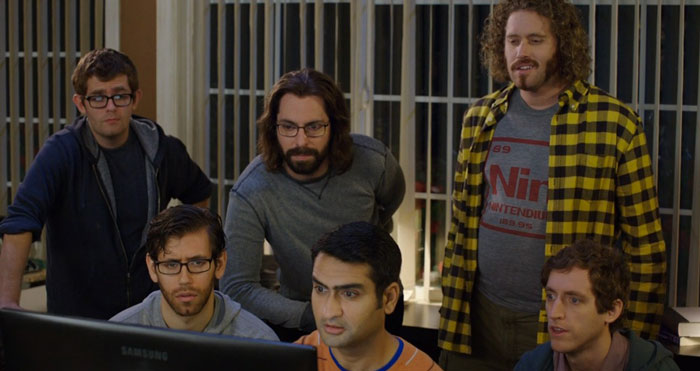 Multiple men looking at computer screens and talking 