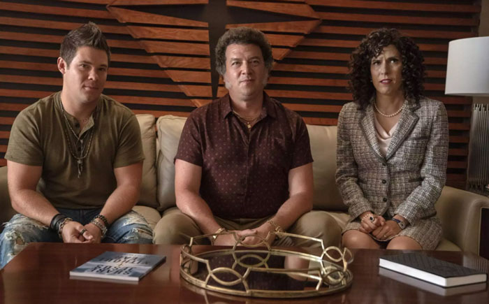 Two men and a woman sitting on a couch and looking at something 