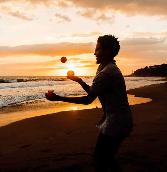 Man juggling three balls in the beach on a sunset 