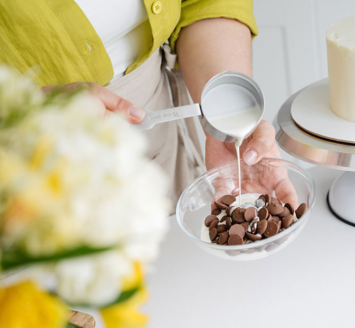 Crop female pouring ganache on chocolate drops