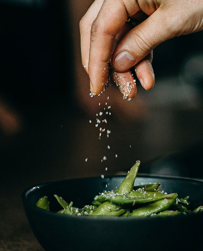 Person pouring seasoning on green beans on bowl
