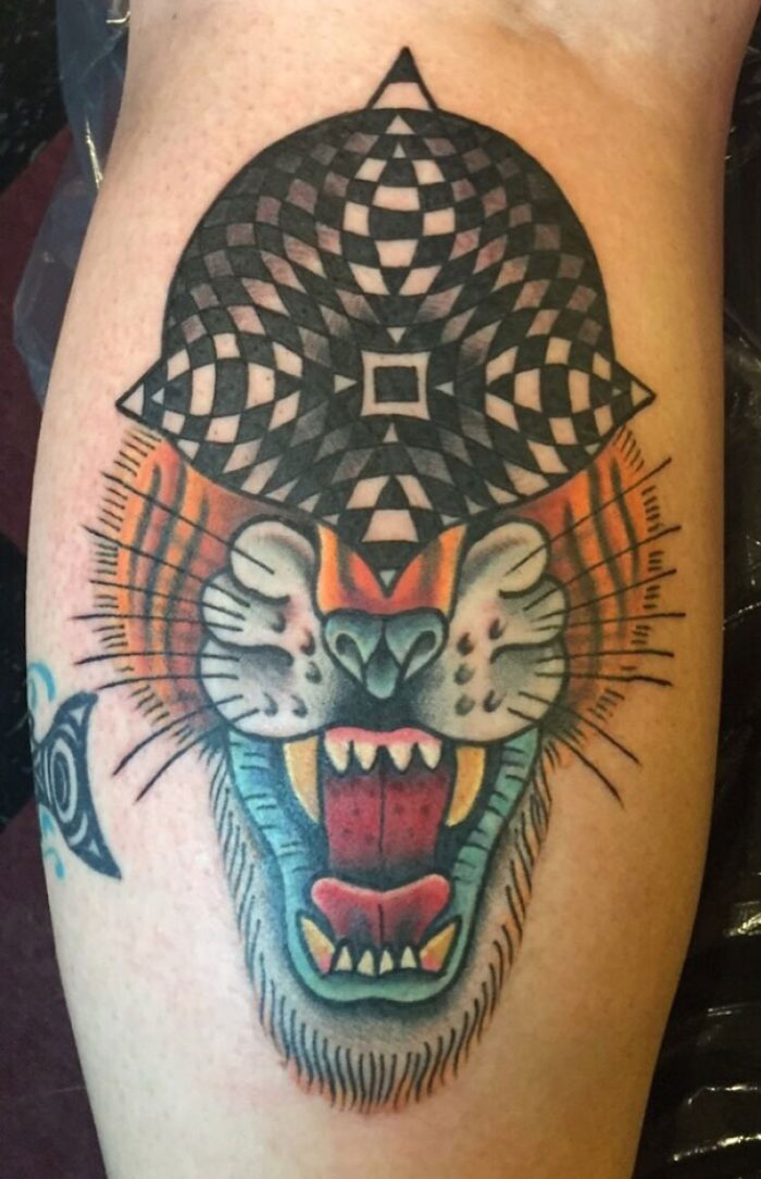 Optical illusion tattoo of a roaring lion with a black and white geometric pattern on its head.