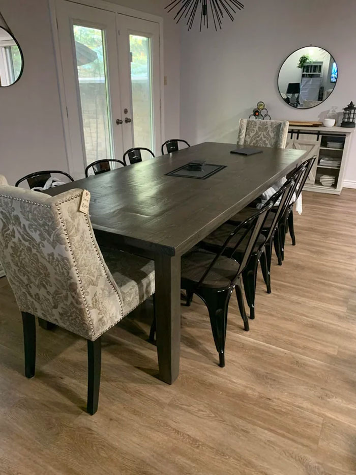 Creative dining room decoration with a large wooden table, a mix of patterned and metal chairs, and modern wall mirrors.