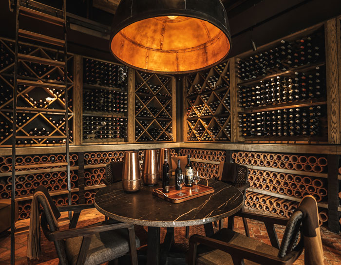 a round table with bottles of wine and glasses near the shelves with wine