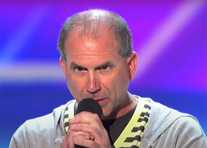 Man delivering a roast, holding a microphone on stage, showcasing the timeless art of roasting in comedy.