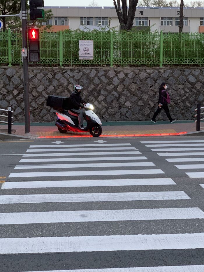 Man with a scooter standing near a pedestrian crossing with a red light under him 