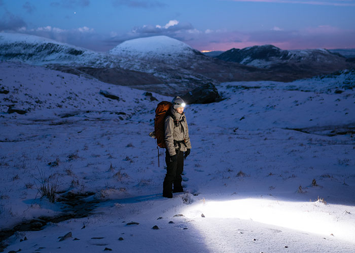Man standing in snowy field with a flashlight on his head