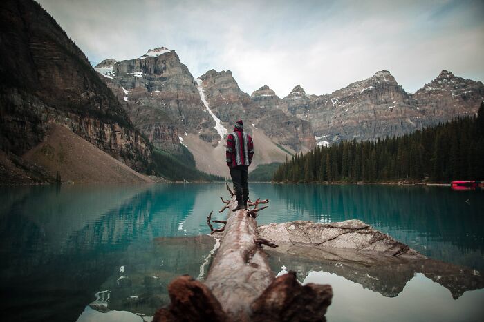 Person Standing On The Log In A Middle Of A Mountain Lake 