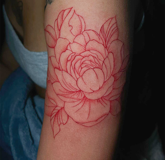 Red ink tattoo of a detailed flower on arm.