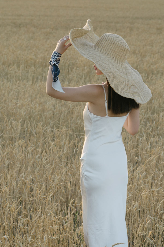 Woman standing and wearing big hat with white dress