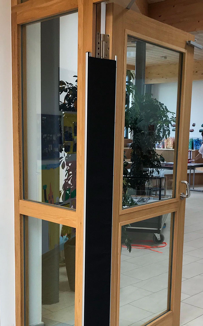 Esta pantalla de tela se coloca sobre la bisagra de la puerta de un jardín de niños para evitar que los niños se aplasten los dedos