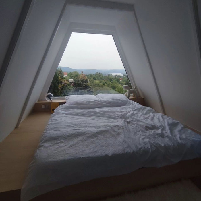 Cozy loft space in a tiny house design with a large triangular window overlooking a scenic landscape.