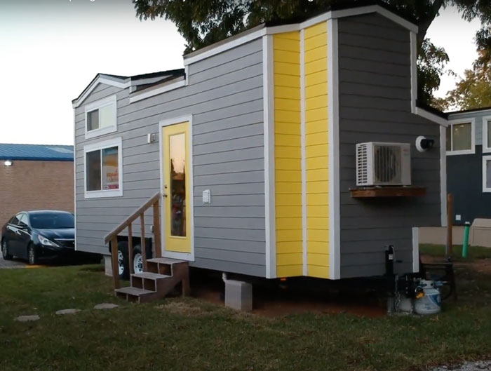 Grey and yellow tiny house design with modern features and compact living space in a peaceful outdoor setting.