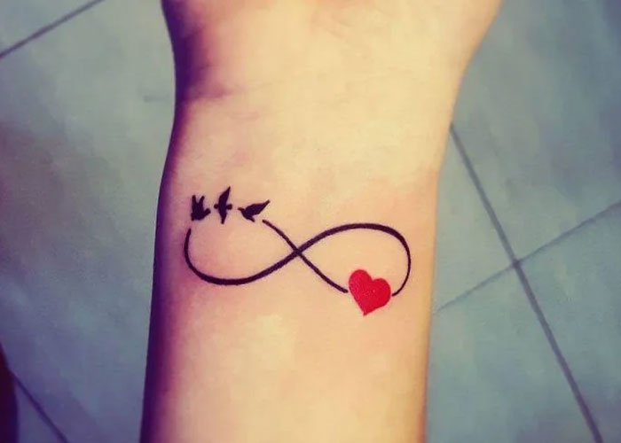 Infinity heart tattoo with birds on a wrist, representing a common tattoo design.