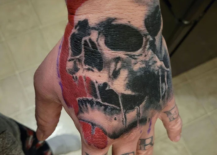 Hand tattoo of a skull design with black and red ink, discussed as lacking creativity.