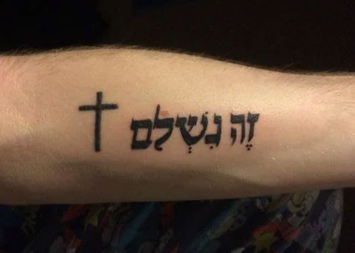 Tattoo design with a cross and Hebrew script on an arm, often seen as lacking creativity.