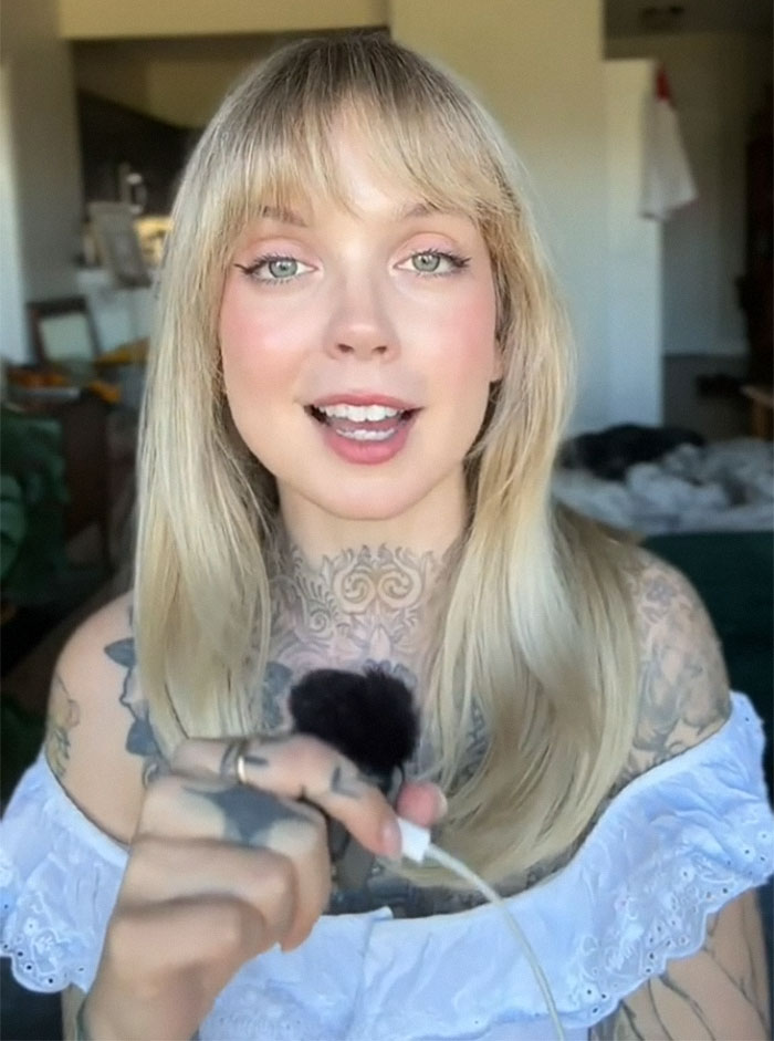 Woman with tattoos sharing regrets, holding a microphone, indoors; her tattoos are visible with long blonde hair. Woman with tattoos sharing regrets, holding a microphone, indoors; her tattoos are visible with long blonde hair.
