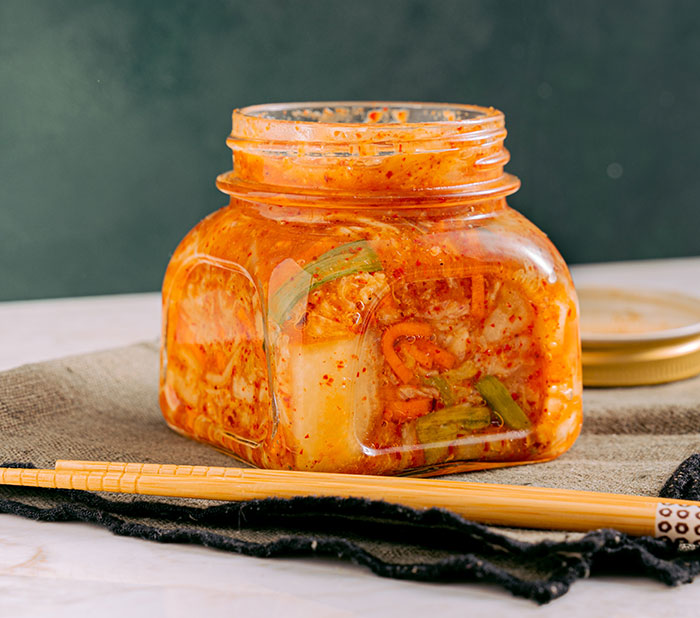 Kimchi in a small jar with chopsticks besides 