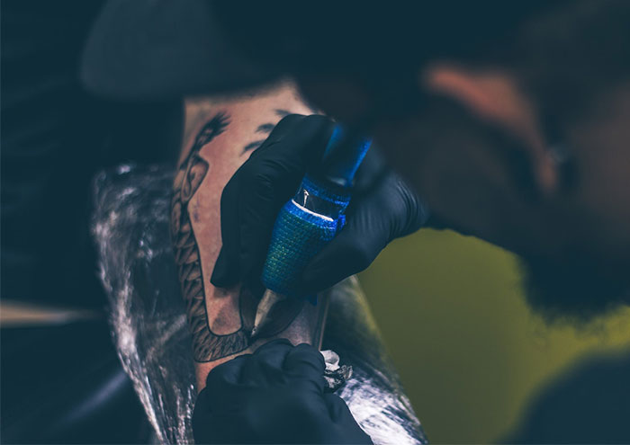 Tattoo artist working on a detailed back piece, highlighting the craft in a dimly lit setting. Tattoo artist working on a detailed back piece, highlighting the craft in a dimly lit setting.