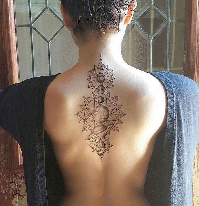 Intricate spine tattoo of geometric and planetary designs on a woman's back.