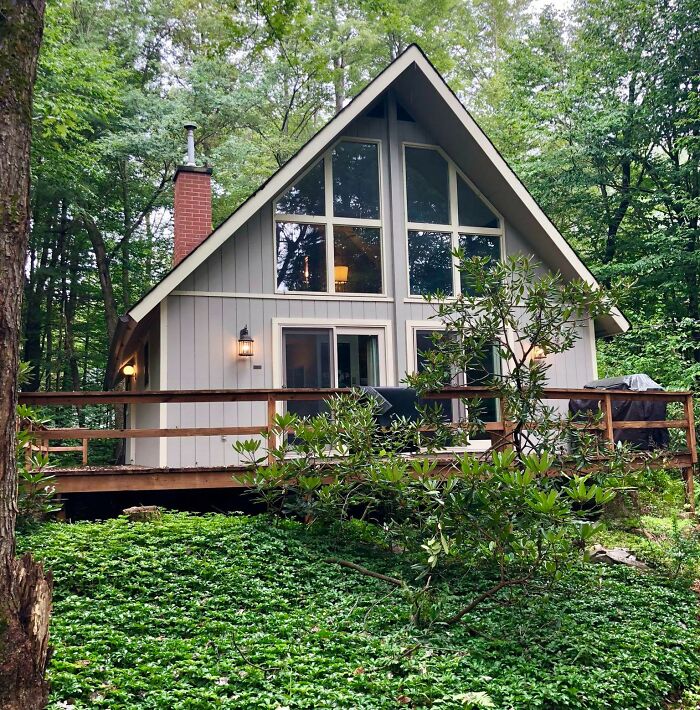 A-frame tiny house design surrounded by lush greenery, featuring large windows and a cozy outdoor deck.