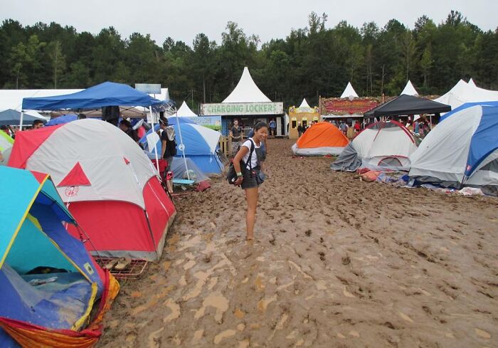 A young woman standing in mud among many tents in TomorrowWorld, 2015