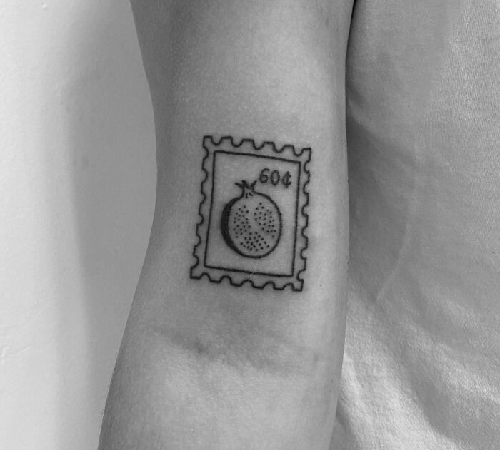 Pomegranate postage stamp tattoo on forearm, showcasing a unique and tasty ink-spiration design.