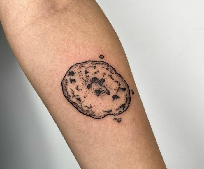 Tattoo of a crispy chocolate cookie on an arm, showcasing creative food-inspired ink designs.