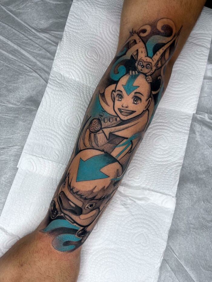 Pop culture tattoo featuring animated characters on a forearm, highlighting vibrant blue and black ink design.