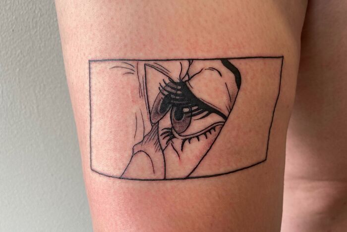 Pop culture tattoo on arm featuring a stylized eye in black ink within a rectangular frame.