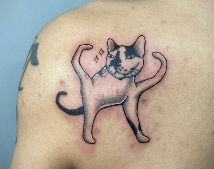 Creative pop culture tattoo of a whimsical cat design on a person's shoulder.
