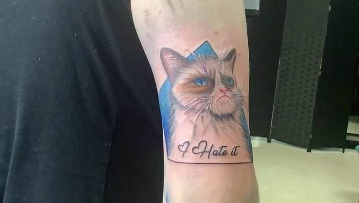 Pop culture tattoo of a grumpy cat with text "I Hate it" on a person's arm.