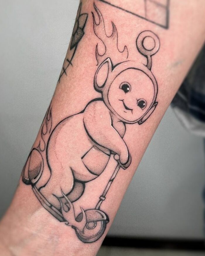 Pop culture tattoo of a baby character with flames, riding a scooter on a person's forearm.