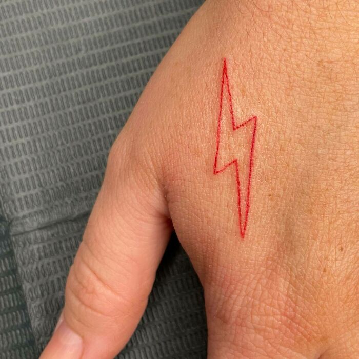 Simple red lightning bolt tattoo on hand