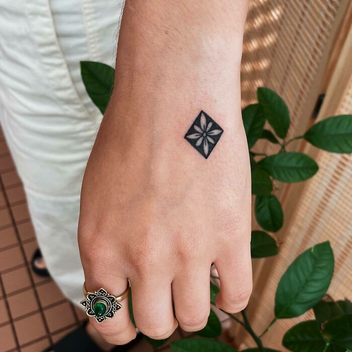 Small black flower in rectangle tattoo on hand