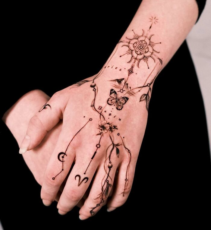 Hand tattoo composition with flowers, butterflies, mountains, and symbols