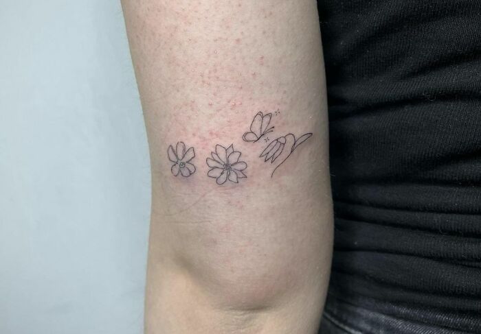 Minimalist flower tattoo on arm with butterfly, showcasing elegance and beauty.