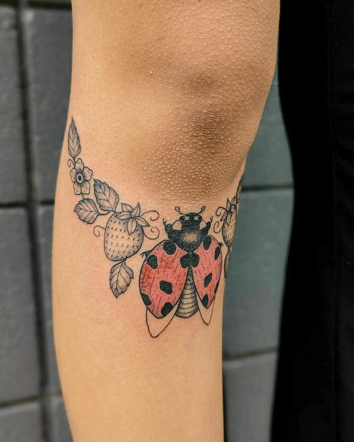 Ladybug with flowers and strawberries below knee tattoo