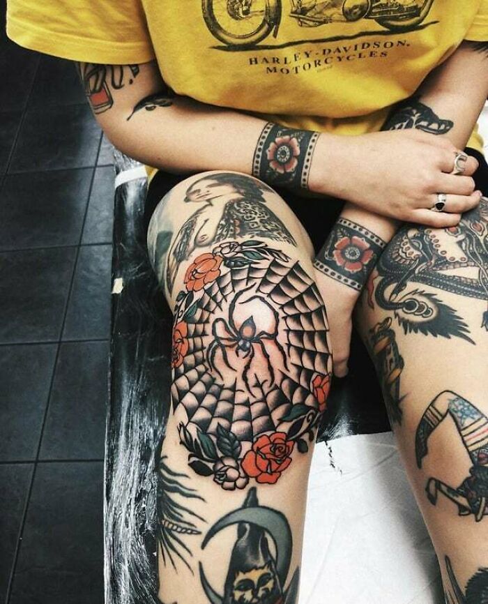 Colorful knee tattoos featuring a spider web design surrounded by roses, showcasing intricate body art.