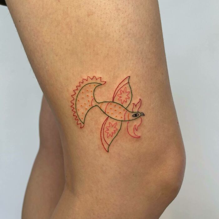 Vibrant bird tattoo design on a knee, showcasing intricate lines and bold colors.